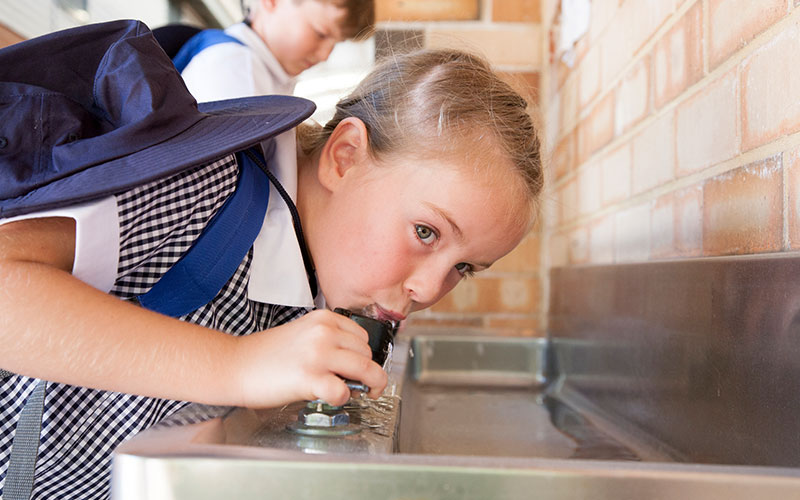 A school child drinking from a drinking fountain