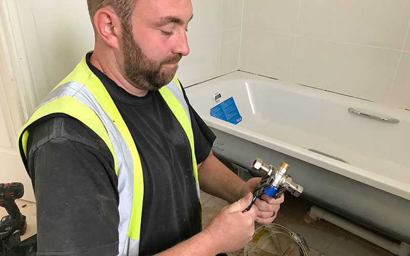 Plumbers installing a TMV under a bath