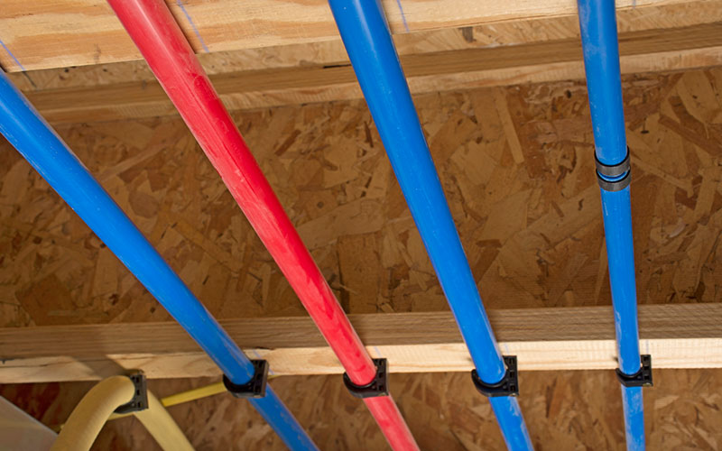 PEX pipes attached to the basement ceiling of a home, angled view.
