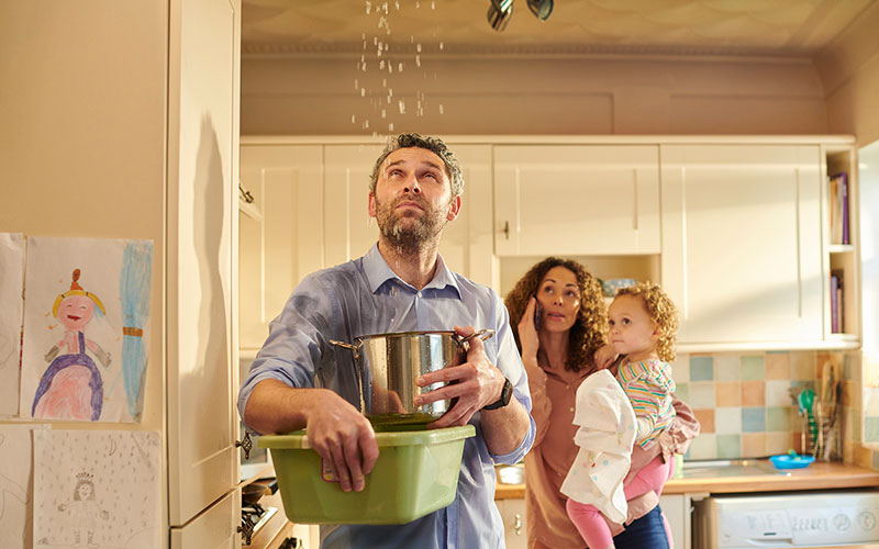 man catching leak in kitchen with bowls